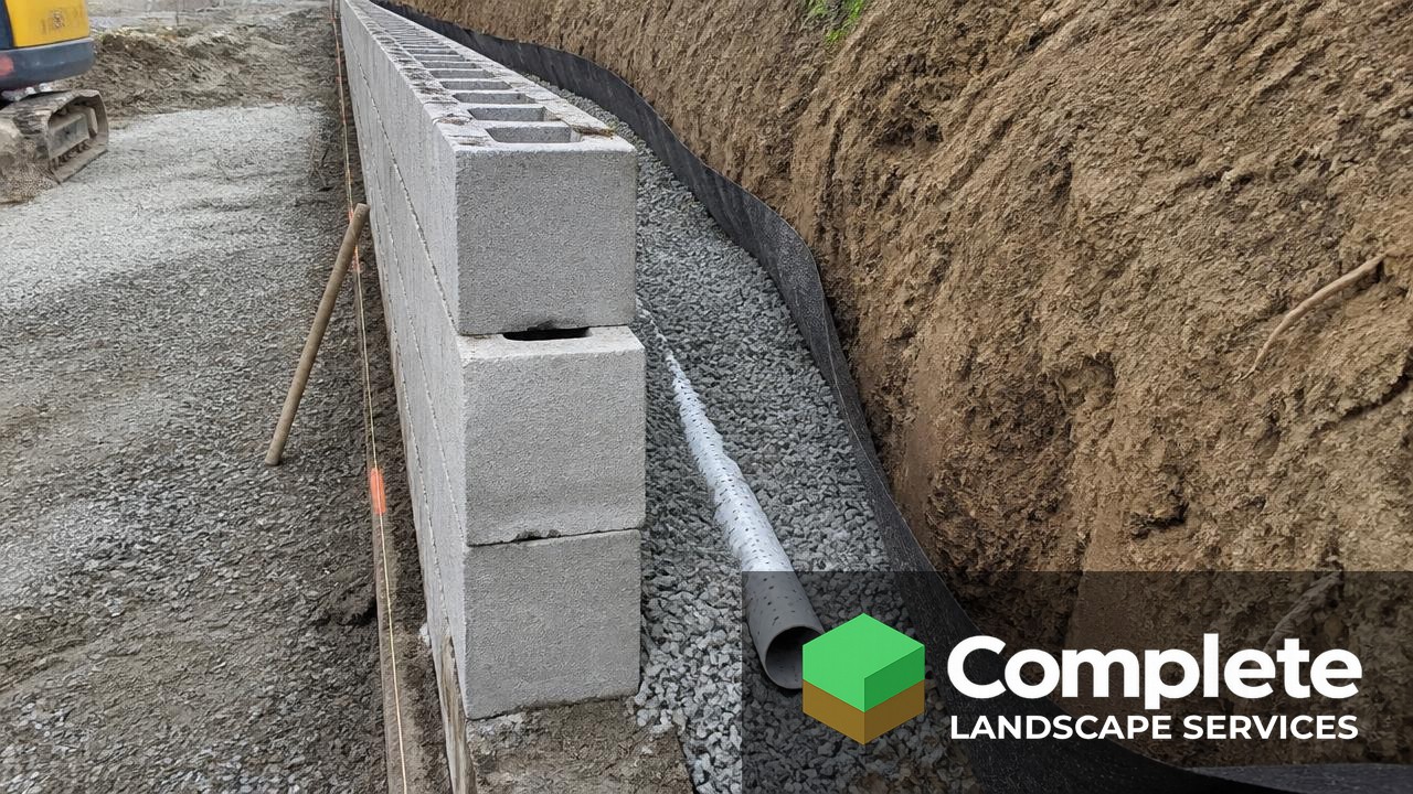 Drainage gravel, filter fabric, and perforated pipe installed behind a partially built block retaining wall