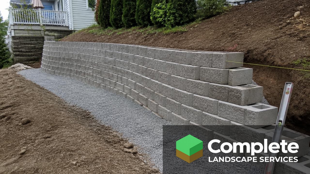Segmental concrete block retaining wall under construction on a sloped backyard with a level and string line